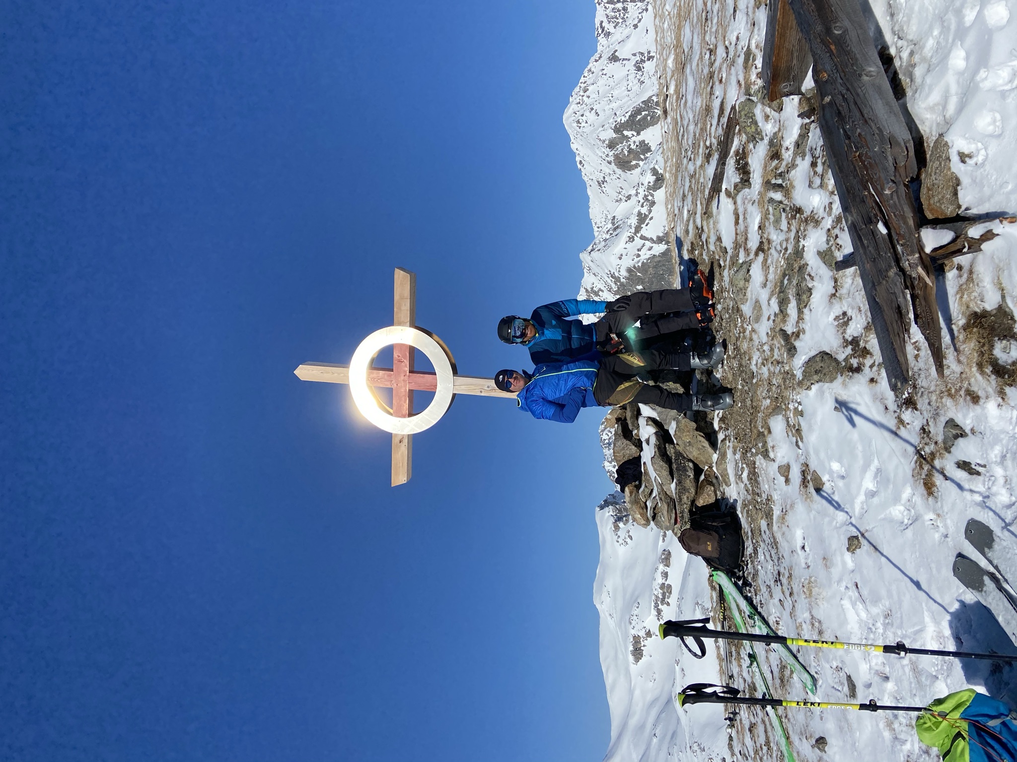 Two ski tourers at the summit cross with a mountain panorama