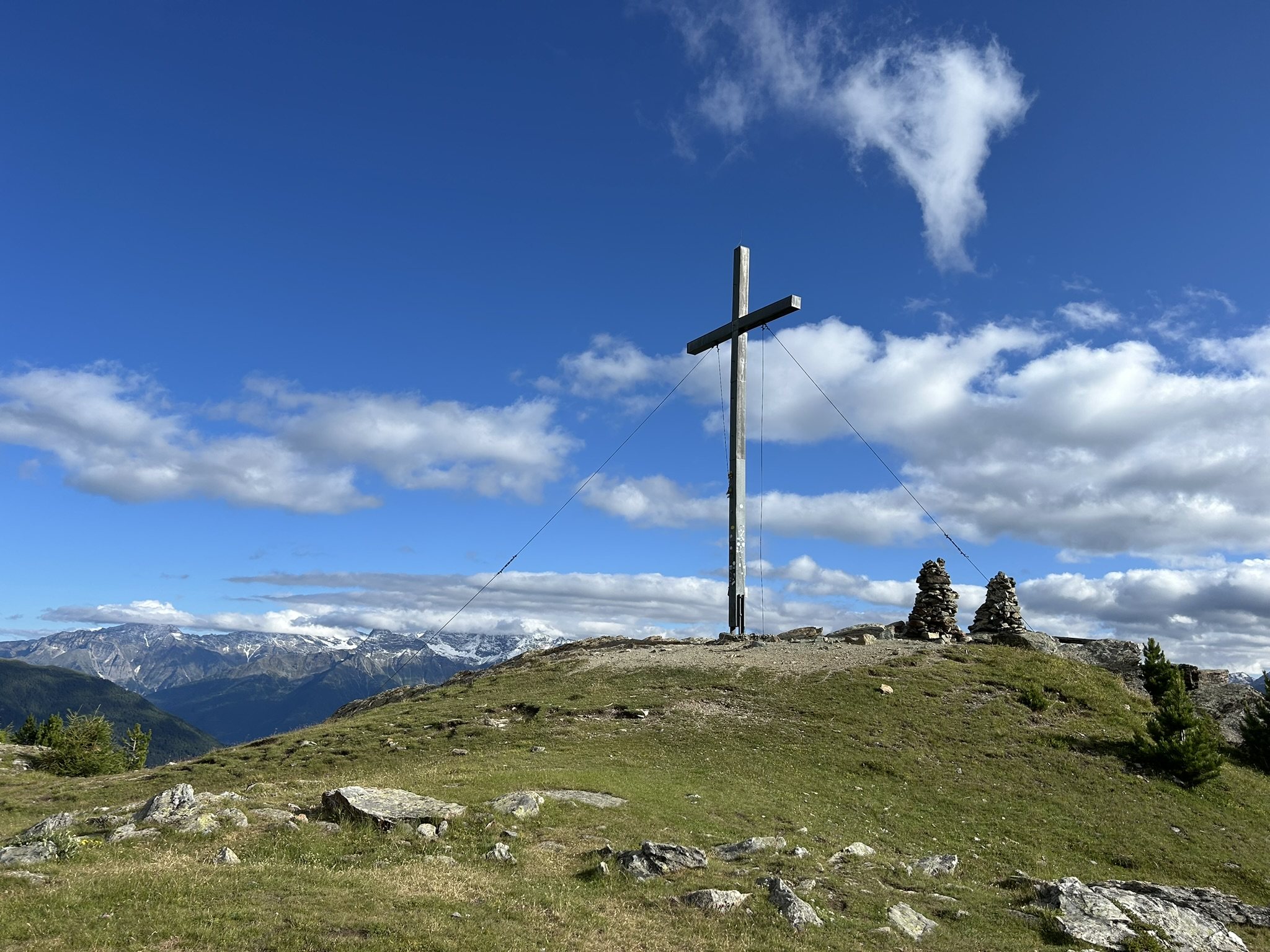 Croce di vetta su un prato montano con vista sulle Alpi